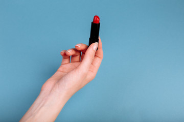 The woman's hand is taking red lipstick. isolated On the blue background