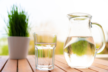 jug with water and a glass on a wooden table on the nature in the garden