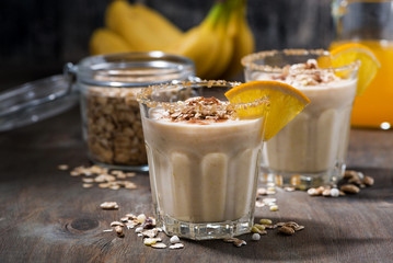 milkshake with oatmeal, banana and orange on dark table, closeup
