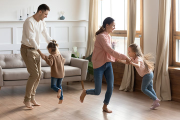 Happy parents dancing with little daughter in living room, excited mother and father holding cute preschool girls hands, moving to favorite music, spending weekend together, funny family activity