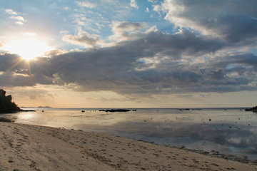 tropical sunset by the sea with clouds reflected in the water