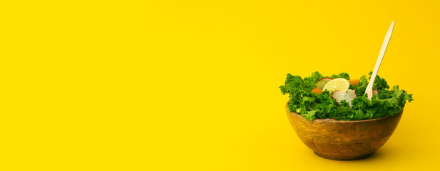 Fresh green salad in a wooden bowl on yellow banner background. Healthy, diet, vitamins, vegetarian,  proper food and lifestyle concept.
