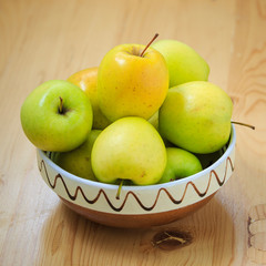 Green succulent apples in a traditional ceramic bowl from romania on a wood table
