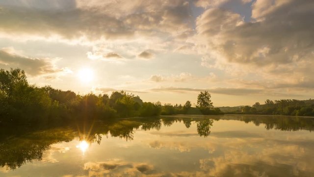 Timelapse of sunrise over lake where the sun rises behind a line of stoma on the shore and gradually changes orange color to daylight with reflection on water surface Hustopece Becvou Czech Republic