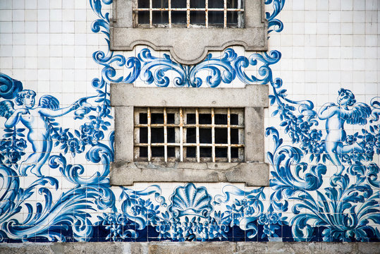 Ventana de piedra enrejada en una fachada hist&oacute;rica de azulejos azules