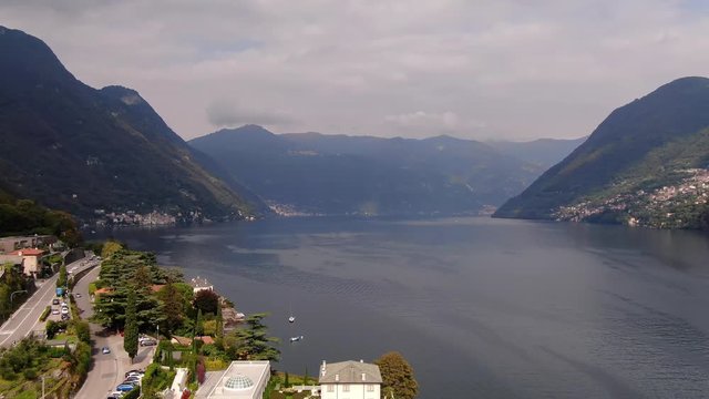 The Vertigo effect (simultaneous zoom in and out effect or Dolly Zoom) while taking aerial shots of the majestic mountains in Italy on blue Lake Como and the village of Laglio in summer sunset days