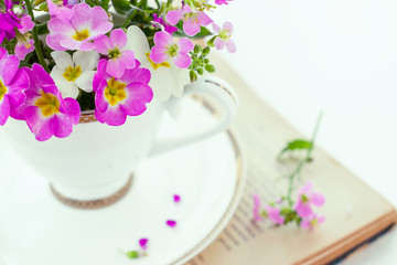 White coffee cup with a bouquet of pink primroses close up and a book on a white background with shallow depth of field.Selective focus