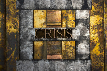 Photo of real authentic typeset letters forming Crisis text on vintage textured grunge copper and black background 