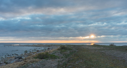 Southern coast of the Finnish Gulf. Rocks covered with green seaweed in the Baltic sea. Smooth transparent reflective water. Orange sunset markings under the low altitude clouds. Estonia, Baltic
