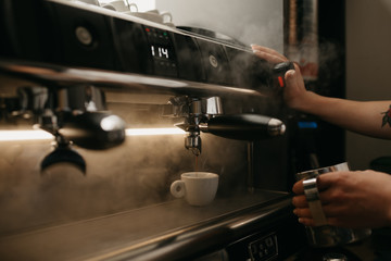 Fototapeta na wymiar A close photo of a professional coffee machine. A barista pouring a coffee in a white cup. Steam around.