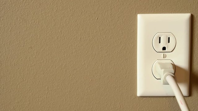 Caucasian hand gripping a three pronged power cord to insert into a power outlet