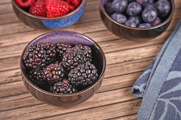 Bunch of ripe blackberry fruits in small bowl on wooden table