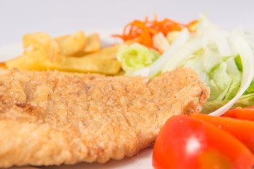 Plate of Roman style hake with chips and salad with lettuce, onion and tomato.