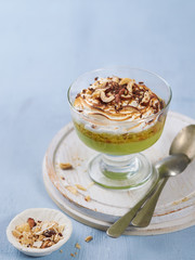 Matcha green tea panna cotta with coconut milk topped with hazelnut and burnt meringue on a light blue background in glass. Concept healthy gluten-free dessert for summer. Copy space, selective focus.