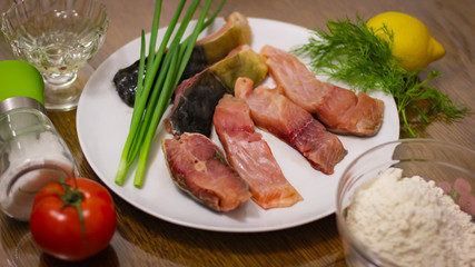 Large Sliced Pieces Of Raw Carp, Tomato, Lemon, Parsley, Green Onions, Lemon, Flour Stand On The Table.
