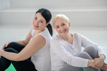 Obraz premium Brunette female and blonde female sitting back to back, smiling