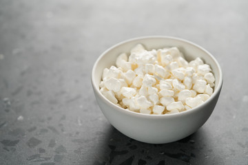 Cottage cheese in white bowl on concrete background with copy space