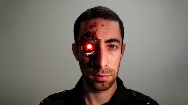 Cinemagraph of red light blinking from the eye of a cyborg humanoid man. Dramatic closeup portrait of a young bearded man with an expressionless face that looking at the camera.