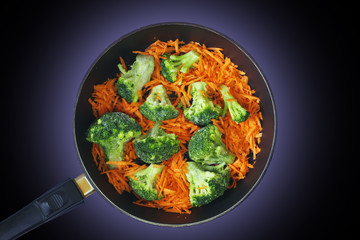 Broccoli and carrots in a pan on a dark background, top view