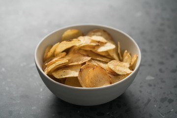 Potato chip slightly sprinkled with black pepper in white bowl on concrete background