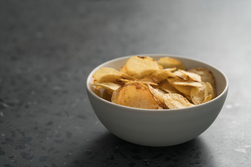 Potato chip slightly sprinkled with black pepper in white bowl on concrete background with copy space