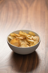 Potato chip slightly sprinkled with black pepper in white bowl on walnut wood background with copy space