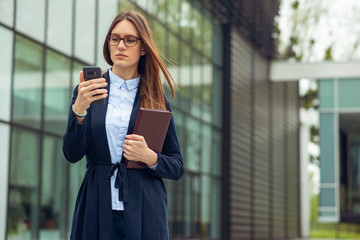Fototapeta premium Executive working with a mobile phone in the street with office buildings in the background