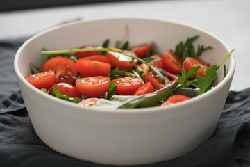 salad with cherry tomatoes and mixed grens in white bowl on concrete background