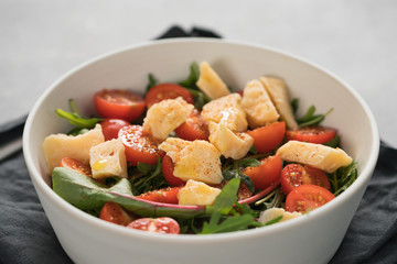 salad with cherry tomatoes, mixed grens and cheese in white bowl on concrete background