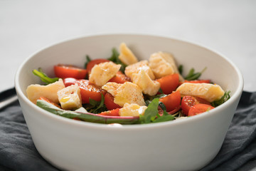 salad with cherry tomatoes, mixed grens and cheese in white bowl on concrete background
