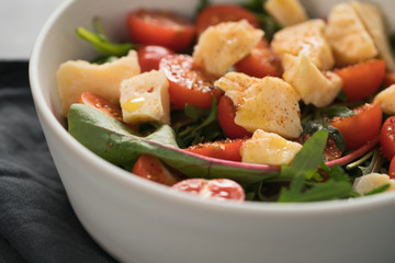 salad with cherry tomatoes, mixed grens and cheese in white bowl on concrete background