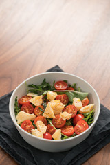 salad with cherry tomatoes, mixed grens and cheese in white bowl on wood table