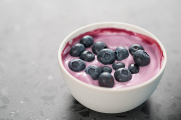 Blueberry yogurt with whole berries in white bowl on concrete background