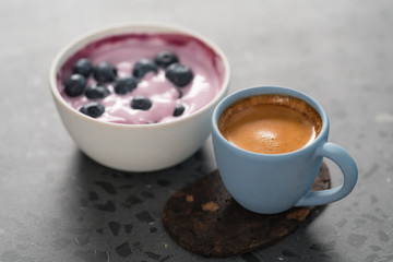 Blueberry yogurt with whole berries and cup of fresh espresso on concrete background
