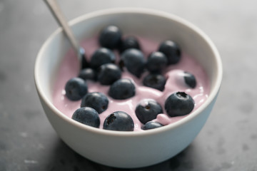 Blueberry yogurt with whole berries in white bowl on concrete background