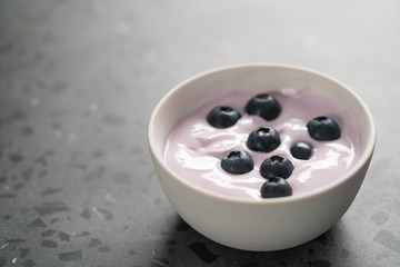Blueberry yogurt with whole berries in white bowl on concrete background