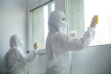 Medical workers in protective clothing and medical masks disinfecting window