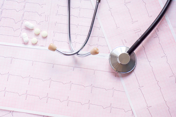 cardiogram with stethoscope, pen, magnifier, pills and glasses lay on a table