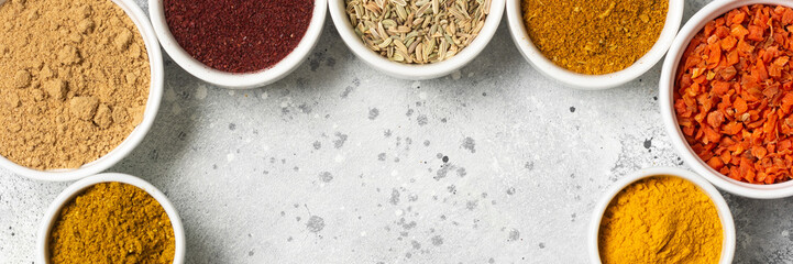 Spices in white bowls on a light gray table. Turmeric, ginger, curry, fennel and sumac in white bowls. Top view with space for text. Banner