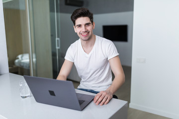 Young attractive smiling man is browsing at his laptop, sitting at home
