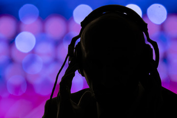 The dark silhouette of a man in headphones on the background of multicolored glare and lights of...