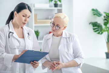 Two female doctors reading the medical history and looking serious