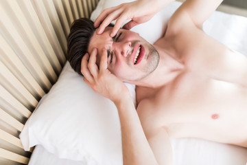 Handsome man wake up with head pain suffers from headache in his bed