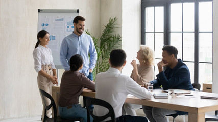 Smiling businessman and businesswoman flip charts presentation new project in boardroom at company meeting. Male and female auditors speaks with diverse partners about business using board and graphs.