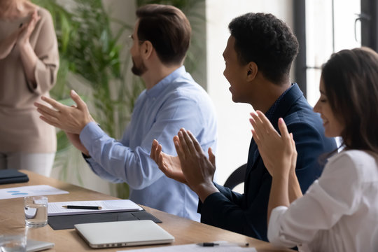 Close up smiling african american businessman clap hands with diverse colleagues congratulating after flip charts presentation in boardroom at meeting. Smiling employee happy about successful project.