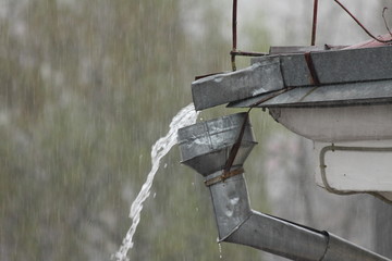 Obraz premium A stream of rainwater from the roof overflows through the funnel of the drainpipe close up, a heavy rain in the city