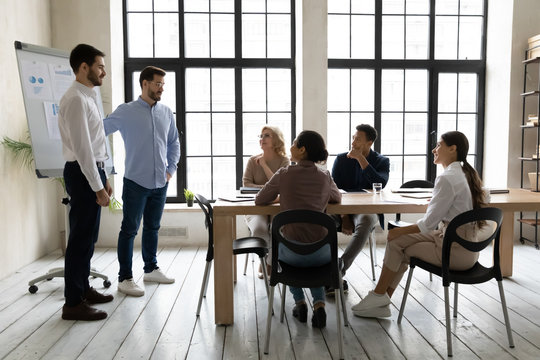 Businessman on behalf of company welcoming young male employee in boardroom at meeting. Introducing hired worker in office getting acquainted supporting new diverse team member on first work day.