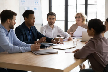 Confident african american businessman talking with young and mature colleagues in boardroom at meeting. Black coach mentor speak with partners negotiating about business project at conversation.