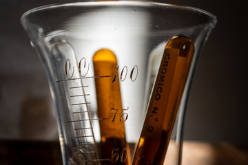 Glass ampoules containing silk sutures from the 1950s in a graduated cup. It is a way of containing...