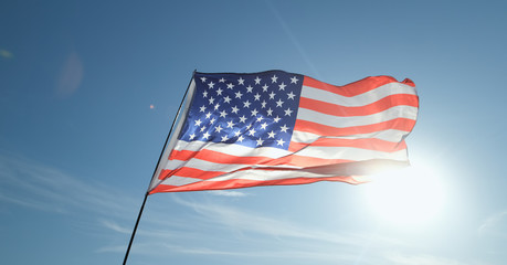 The USA flag flaps in the wind against a blue sky.